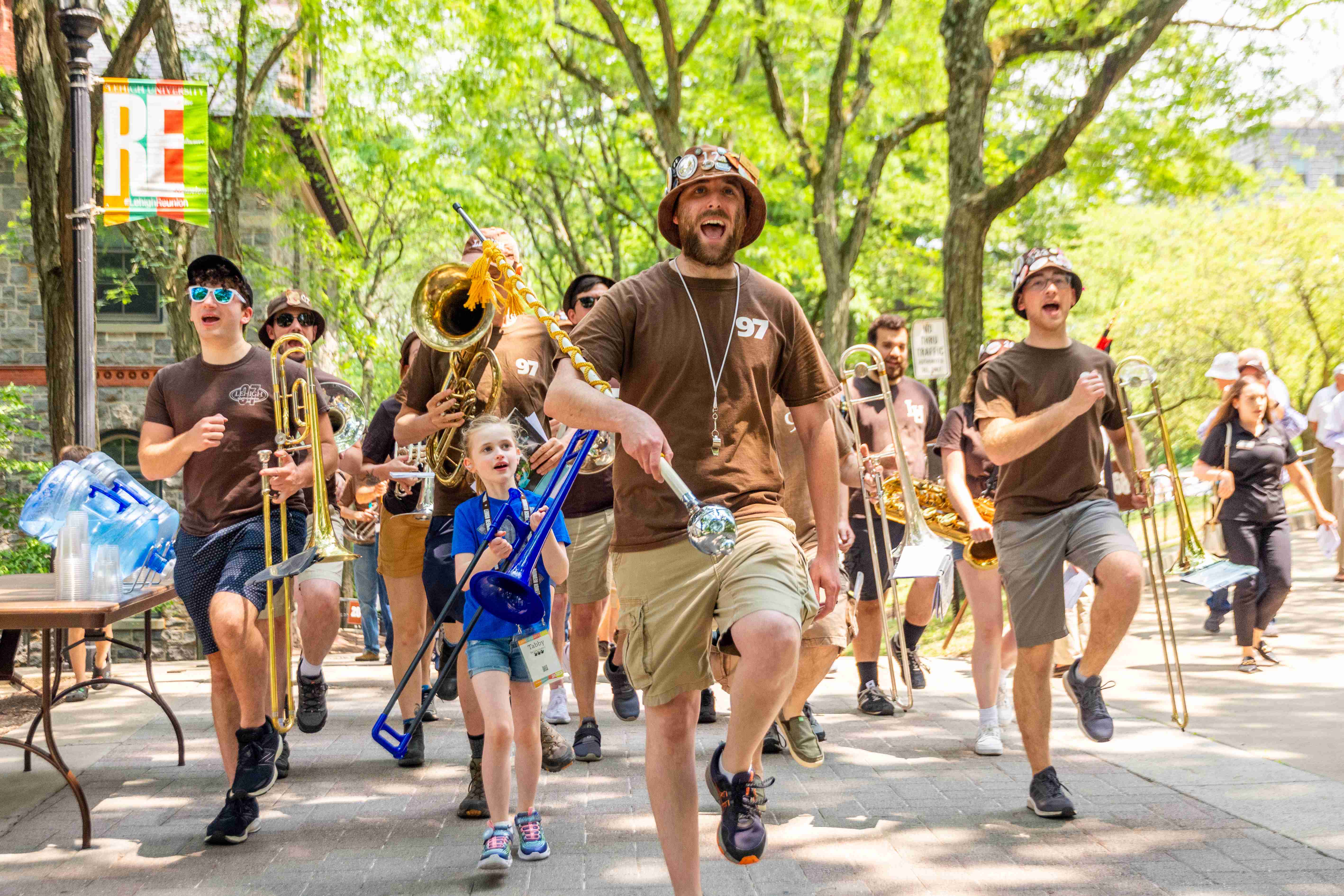 Marching 97 alumni marching and singing alongside a little girl with a trombone