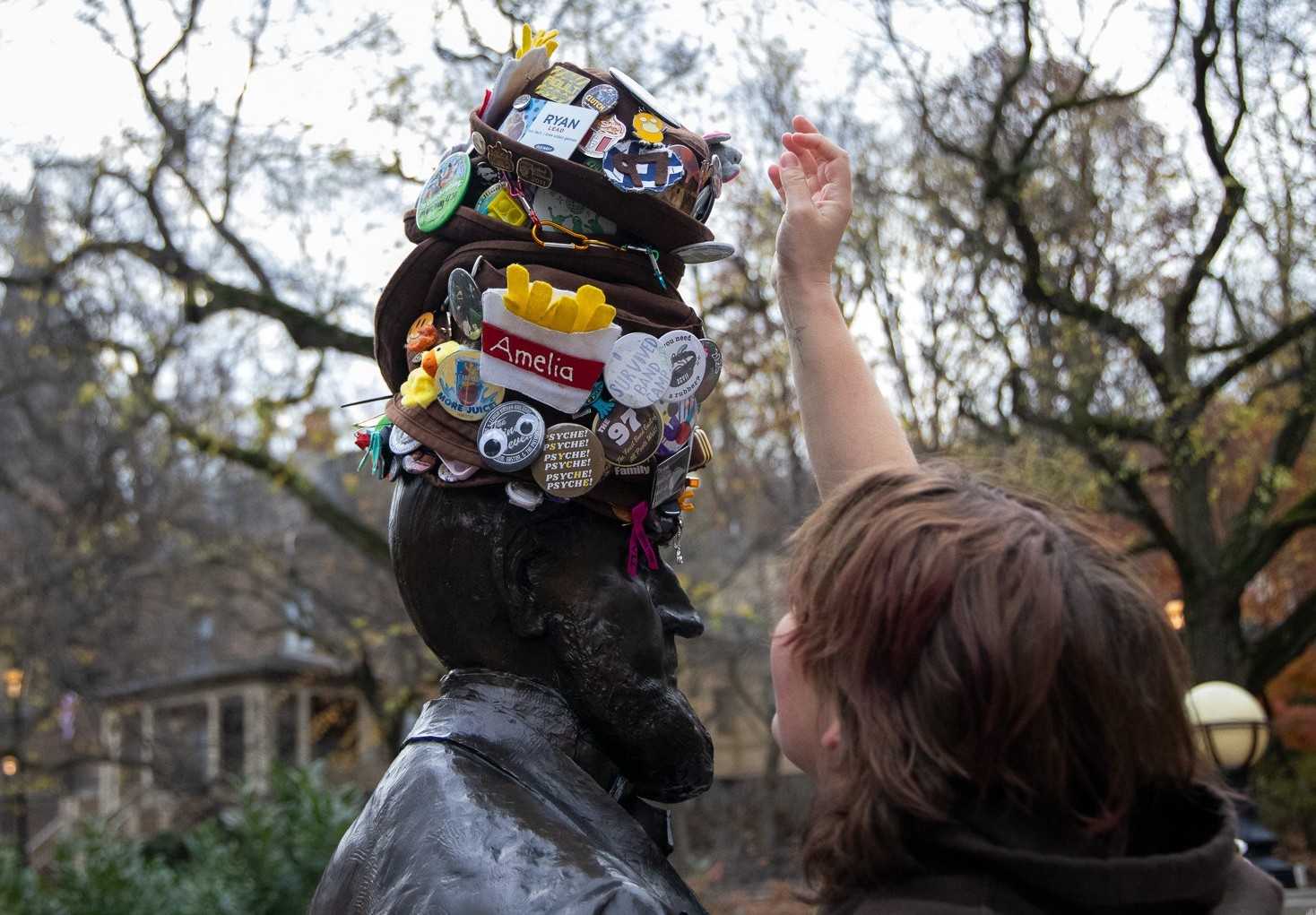 A band member adds their hat, or 'dink', to the stack on top of a statue of Asa Packer